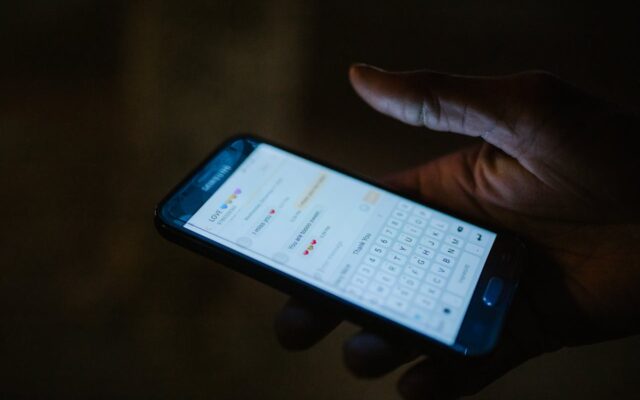 Main tenant un smartphone affichant une notification illustrant les arnaques par SMS et phishing